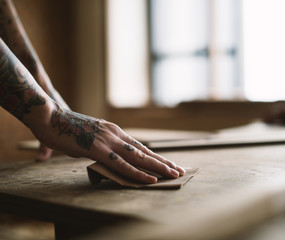 Hands with tattoo using sandpaper on a wood