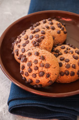 Cookies with chocolate chips in a brown plate on a napkin. White stone background.