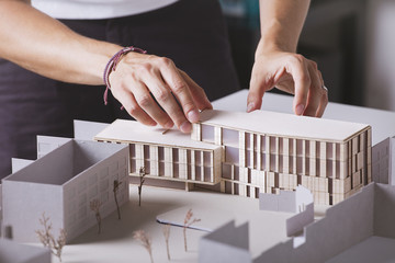 Close up of hands of young architect working on a building project with a scale model.
