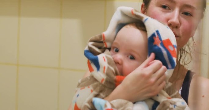 mother holding cute happy glad baby boy wrapped blanket bathing bath bathroom looking mirror smiling young woman adorable child interested big eyes chubby cheeks motherhood health caring washed body
