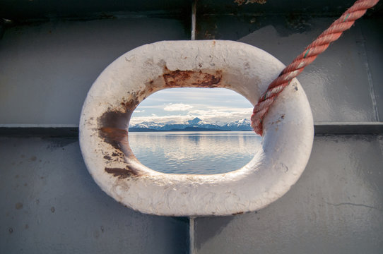 A view of the ocean and Alaskan mountains through a ship's porthole