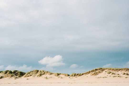 Man and his dog walking up sand dunes on a beach