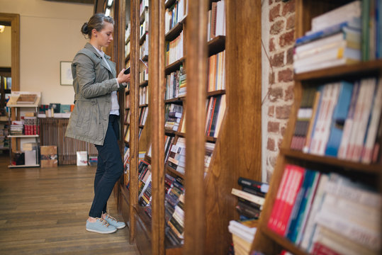 Woman in a library reading by the bookcase