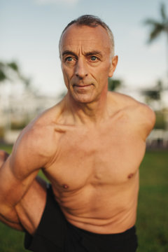 Muscular, fit senior man doing yoga outside in morning sunlight