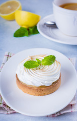 Delicious Lemon tart tartlet with meringue and mint in white plate on blue stone concrete table background. Copy space