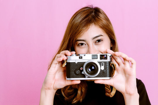 Fashion photo of young girl posing with vintage camera in hand on pink background