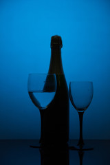 Glasses of champagne and a bottle of wine on a black background with blue light