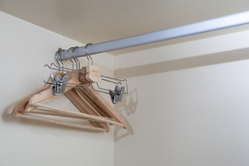 A close-up of wooden empty beige hangers for storing clothes and trousers hang in a row on a mettalical racking inside a beige cabinet