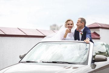 Happy newlyweds hug in a cabriolet on their wedding day