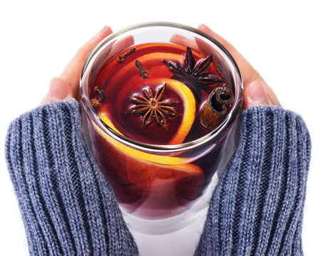 Hands holding a glass cup with mulled wine, spices, orange, anise and cinnamon sticks on white background.