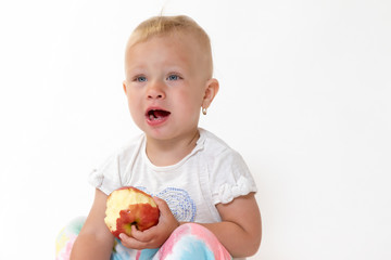 Studio shot of sitting cool toddler girl holding red apple and looking on the side of the camera with an open mouth. 