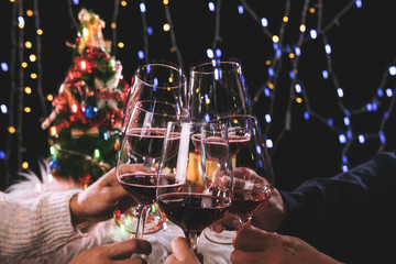 Friends celebrating Christmas or New Year eve party, cheering with wine, christmas lights decoration background, christmas atmosphere