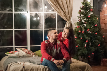 Obraz premium Beautiful happy young family celebrating Christmas together. Lovers on the New Year together in an apartment in the Loft style. Bedroom apartment Loft decorated in New Year's style.