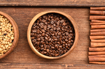 Close up of coffee beans in wooden bowl and cinnamon on wood background