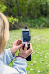 A blonde woman using a phone takes a photo of a beautiful landscape