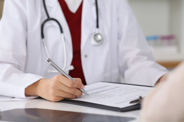 Close up of a female doctor filling up  an application form while consulting patient