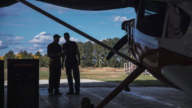 Two men standing in hangar and talking with each other.