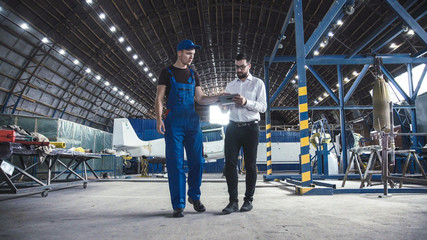 Mechanic and flight engineer having a discussion together as they stand in aircraft in a hangar.
