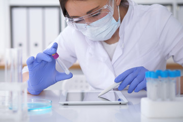 Close-up of professional female scientist in protective eyeglasses making experiment with reagents...