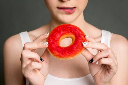 Woman holding calorie bomb donut on gray background. Junk food concept
