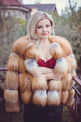 Middle age sexy woman in red lingerie body and fur fox coat, in cozy home atmosphere at winter warm evening. Concept of femininity and tenderness after 30-40 years