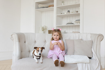 Little charming girl in pink dress and adorable dog posing on couch looking at camera. 
