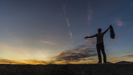 Fototapeta na wymiar Man in casual clothes holding his sweater standing on a wall against a sunrise