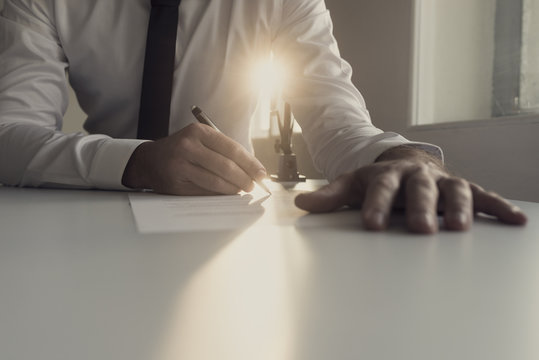 Businessman in white shirt signing document backlit by a shaft of bright sunlight