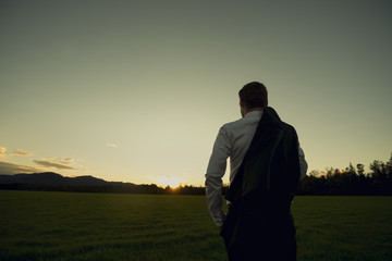 Businessman in elegant suit with his jacket hanging over his shoulder standing in mown field
