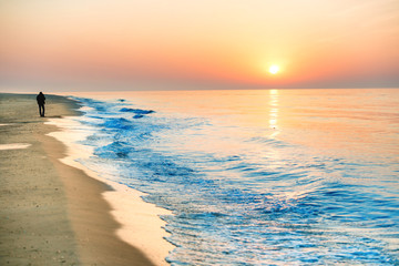 Sunset on the beach with long coastline and man silhouette on it, sun and dramatic sky 