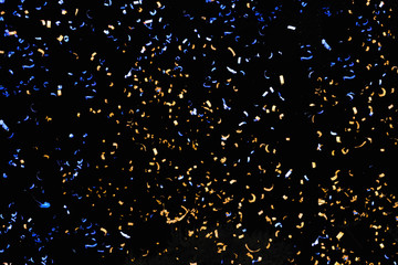 Confetti fired in the air during a beach party. Only confetti on black background of the night. Confetti blue and yellow