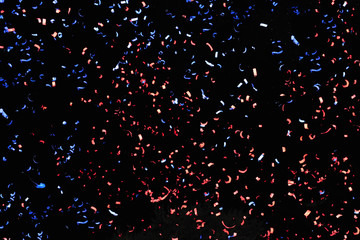 Confetti fired in the air during a beach party. Only confetti on black background of the night. Confetti blue and red