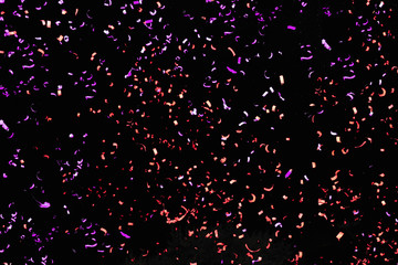 Confetti fired in the air during a beach party. Only confetti on black background of the night. Confetti purple and red