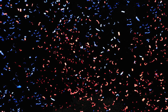 Confetti Fired In The Air During A Beach Party. Only Confetti On Black Background Of The Night. Confetti Blue And Red