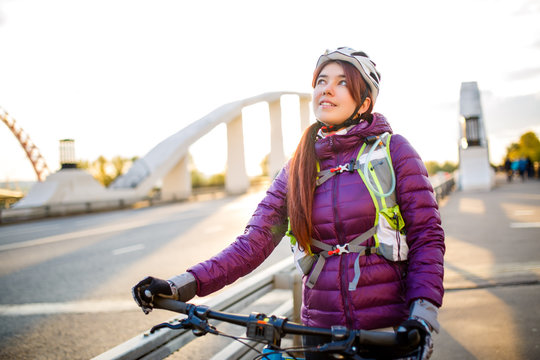 Photo of sports girl in helmet on bicycle on bridge in city