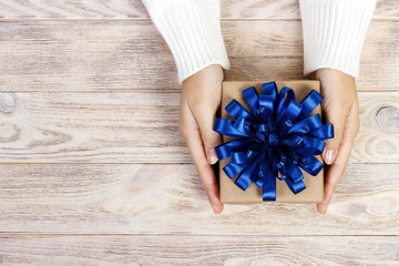Woman's hands hold christmas or new year decorated gift box. gift box with a big blue bow