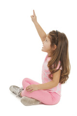 Beautiful little girl sitting on floor pointing with finger. Isolated on white background 