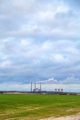 Smoking chimneys of an old factory on the background of green grass and autumn sky in the clouds