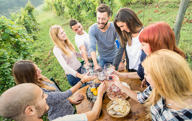 Young friends having fun outdoor clinking red wine glasses - Happy people eating grape and drinking at harvest time in farmhouse vineyard winery - Youth friendship concept on bright candid filter