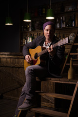 young man with  guitar sits on  wooden stairway in  bar