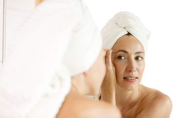 Woman shaping of her eyebrows with tweezers looking in mirror