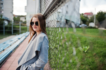 Girl in gray coat with sunglasses at small street stadium.