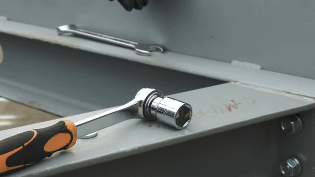 A worker puts his hands on top of a socket wrench lying around a work area.