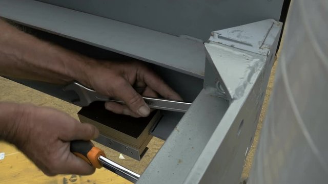 A worker tightens a bolt with a monkey wrench and a socket wrench. Close up.