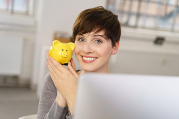 lächelnde frau sitzt am computer zeigt ihr sparschwein