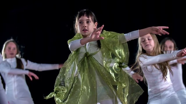 Young girls are dancing to a modern routine on stage. They are wearing white costumes.
