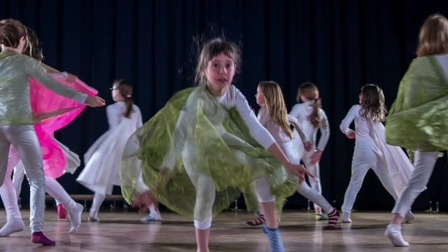 Lots of girls are performing on stage. They're wearing white costumes and green and red capes. They're touching each other's hands in one part of the routine.