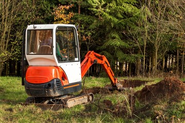 Work on the construction site of an ecological house. The excavator adjusts the terrain. A small digger in the garden.