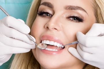Young beautiful woman with beautiful white teeth sitting on a dental chair. The dentist cures her...