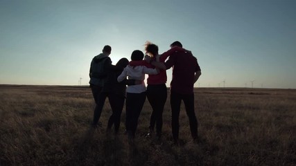Group of five people warming against wind farm at sunset movement stabilized shot